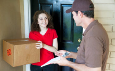 Delivery man brings a package to a customer's door and waits for a signature.